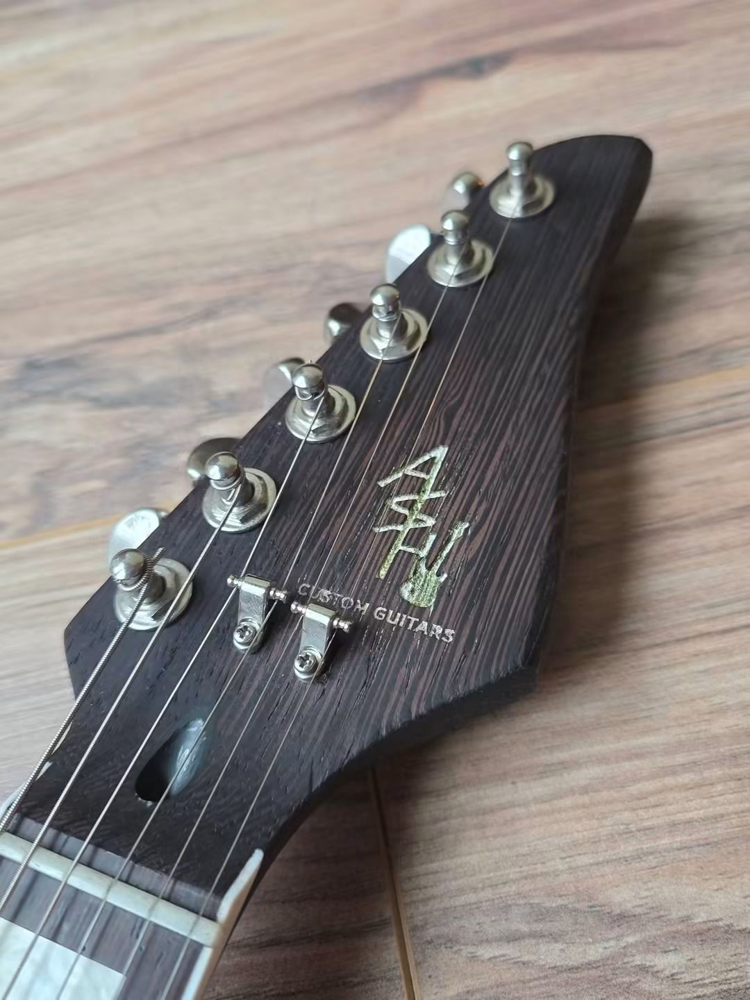 Ash symbol on a dark wood guitar headstock beside chrome tuning pegs